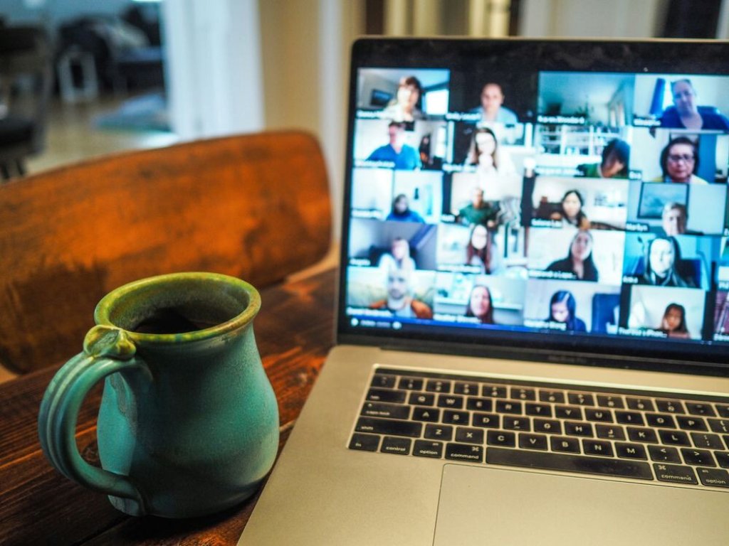 Coffee and Laptop showing a video conference on a wooden desk.